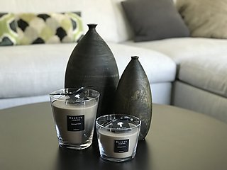 Duftkerzen von Baobab und dunkle Holzvasen auf dem Couchtisch vor dem hellen Sofa.