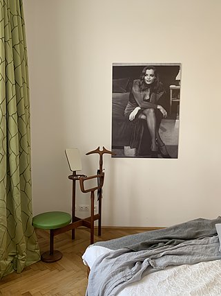 Schlafzimmerecke mit Stummer Diener, grünem Vorhang und Schwarz-Weiß-Porträt an der Wand.