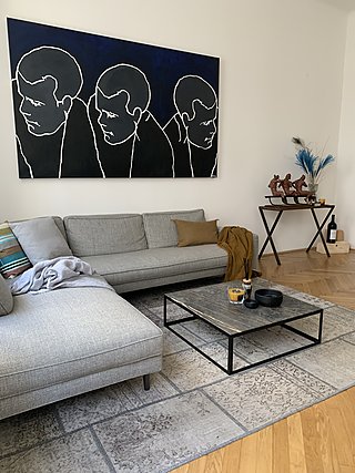 Graues Ecksofa mit Couchtisch aus Naturstein und Metall unter großem Kunstgemälde.