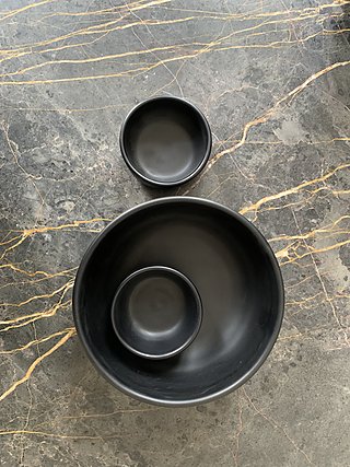 Dunkle Keramikschalen auf einer Marmorplatte mit goldenen Adern.