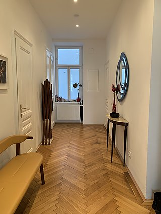 Eingangsbereich mit Fischgrätparkett, skulpturalem Garderobenständer und Konsolentisch unter einem Kunstspiegel.