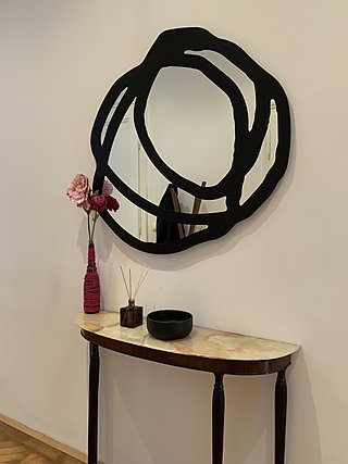 Konsolentisch mit Marmorplatte, Blumenvase und Raumdiffusor unter einem schwarzen Kunstspiegel.