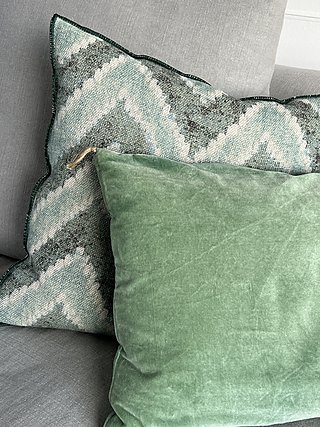 Grünes Samtkissen und gemustertes Zierkissen in Grüntönen auf dem Sofa.