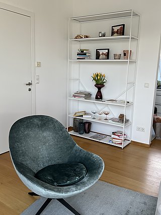 Grüner Samtsessel vor einem weißen Metallregal mit Büchern, Tulpen und Dekoration.