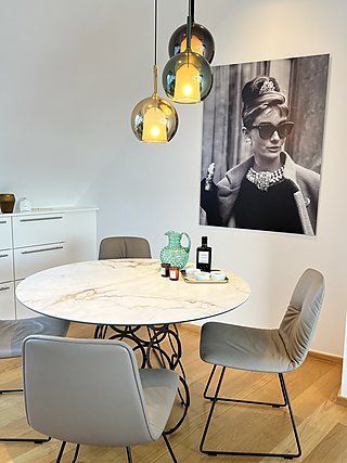 Runder Marmortisch mit Polsterstühlen, bunten Glaspendelleuchten und großem Kunstdruck.