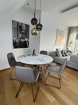 Offener Wohn-Essbereich mit Marmortisch, Pendelleuchten, Sofa und Dachschräge.