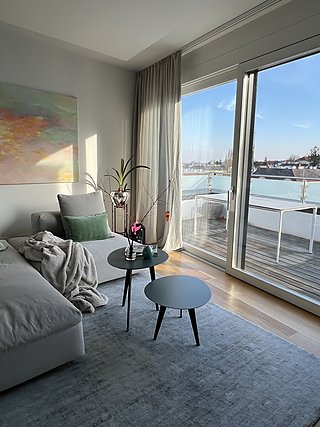 Sofa mit Beistelltischen und blauem Teppich vor der Terrassentür mit Stadtblick.