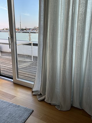 Leinenvorhang an der offenen Terrassentür mit Blick auf die Holzterrasse.