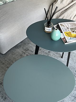 Zwei runde Beistelltische in Petrol mit Raumduft und Vase neben dem Sofa.
