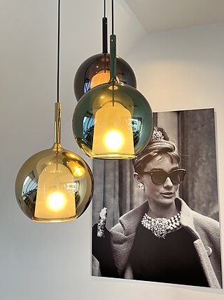 Drei bunte Glaspendelleuchten in Gold und Grün vor einem großformatigen Kunstdruck.