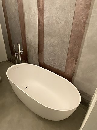 Weiße freistehende Badewanne mit Standarmatur vor einer Wand mit venezianischer Tapete.