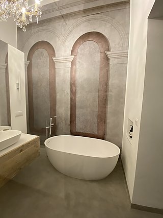 Badezimmer mit freistehender Wanne, Tapete mit Bogenarkaden, Kristallkronleuchter und Holzwaschtisch.