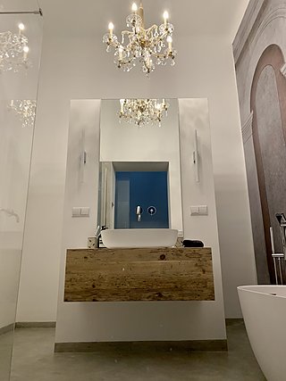 Waschtisch aus Altholz mit Aufsatzbecken unter einem antiken Kristallkronleuchter und großem Spiegel.