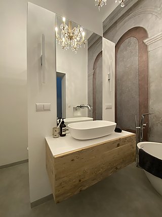 Nahansicht des Waschtischs aus Altholz mit weißem Aufsatzbecken, Wandarmatur und Tapete mit Bogenarkaden.