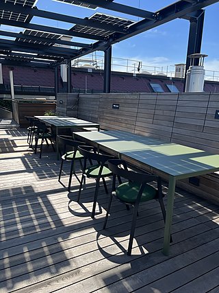 Outdoortische mit grünen Hockern auf der Dachterrasse unter einer Solarüberdachung.