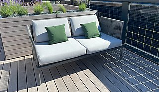 Zweisitzer Sofa mit weißen Polstern und grünen Kissen neben Pflanzbeeten.