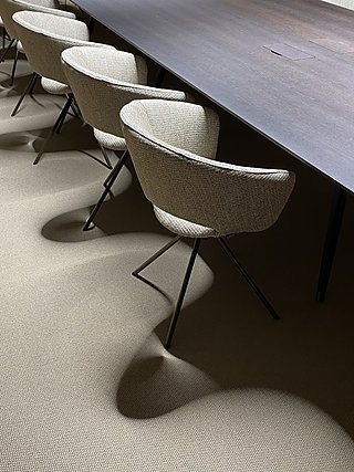 Helle Polster-Drehstühle am dunklen Konferenztisch auf gewebtem Teppichboden.