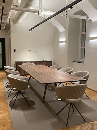 Besprechungsraum mit Nussholztisch, hellen Drehstühlen und Teppich auf Parkettboden.