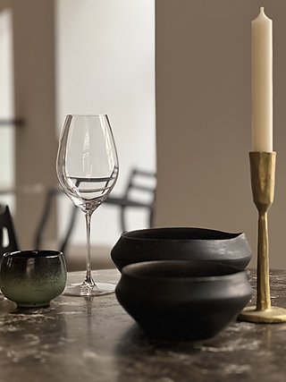 Weinglas, schwarze Keramikschalen und Messingkerzenhalter auf der Steinplatte.