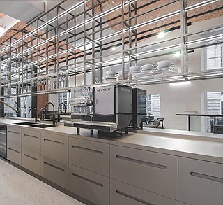 Filigrane Küchenzeile aus Metall mit Kaffeemaschinen, offenem Regal und Spiegelwand.