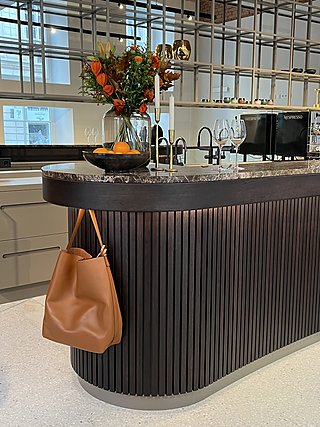 Gerundetes Ende des Barmöbels mit Lamellenverkleidung, Steinplatte und Ledertasche am Haken.