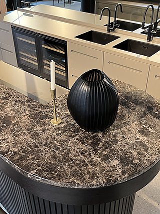 Dunkle Marmorsteinplatte der Bar mit schwarzer Vase und Kerzenhalter, Küchenzeile dahinter.