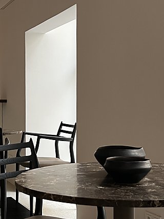 Runder Marmortisch mit Keramikschale, schwarzer Sessel vor einem beleuchteten Durchgang.