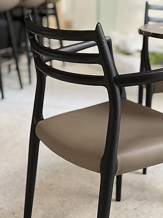 Detailansicht eines schwarzen Holzstuhls mit Ledersitzfläche in Taupe.