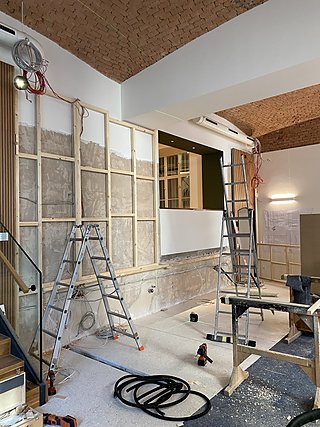 Baustelle während der Montage der Spiegelwand mit Leitern und Werkzeug im Raum.