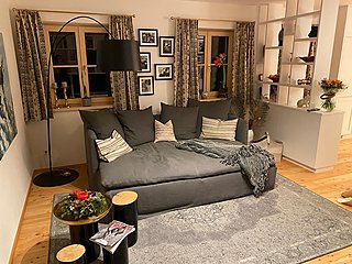 Gemütliches Wohnzimmer mit tiefem Sofa, Stehlampe, Bildern und gemusterten Vorhängen.