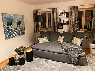 Wohnzimmer mit dunklem Sofa, Alpenmotiv-Gemälde und Baumstamm-Beistelltischen.