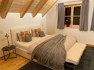 Helles Schlafzimmer mit weißem Polsterbett, orangefarbenen Kissen und Sitzbank.