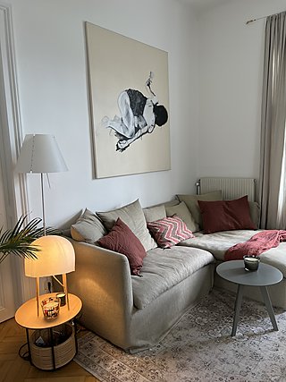 Ecksofa in Beige mit roséfarbenen Kissen, Stehlampe und großformatigem Kunstwerk im Altbau.