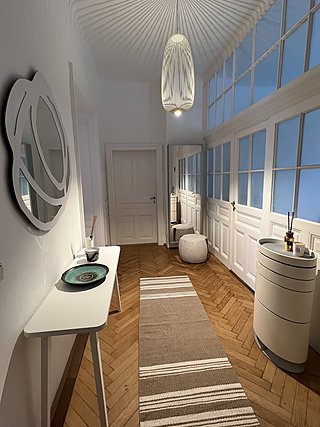 Langer Flur mit Sprossenfenstern, Pendelleuchte, Designspiegel und Konsolentisch auf Fischgrätparkett.