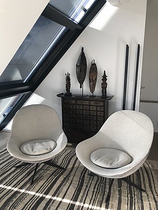 Zwei moderne Drehsessel in Grau vor einem antiken Schubladenschrank mit afrikanischen Masken unter der Dachschräge.