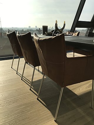 Lederstühle am Esstisch vor raumhoher Verglasung mit Panoramablick über Wien.