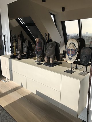 Sammlung afrikanischer Masken und Skulpturen auf einem weißen Sideboard vor der Dachverglasung.