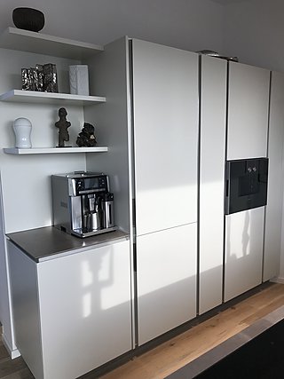 Weiße Küchenzeile mit Einbaukühlschrank, Kaffeemaschine und offenen Regalen.