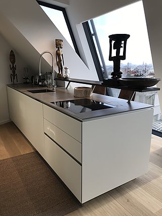 Weiße Kücheninsel mit Steinarbeitsplatte, Kochfeld und Spüle unter dem Dachfenster.