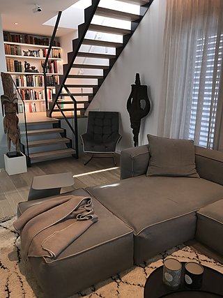 Wohnbereich mit großem Sofa, offener Treppe, Bücherregal und Lounge-Sessel.