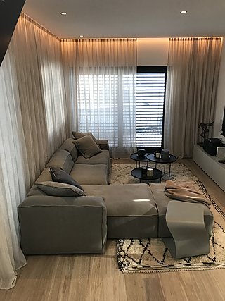 Großzügige Sofalandschaft in Grau mit Kissen, Vorhängen und indirekter Deckenbeleuchtung.