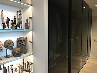 Beleuchtete Regale mit afrikanischer Kunstsammlung neben einem Glasschrank im Vorzimmer.