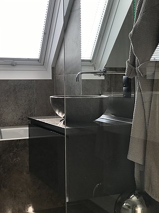 Dunkler Steinwaschtisch mit Aufsatzbecken und Wandarmatur unter dem Dachfenster.