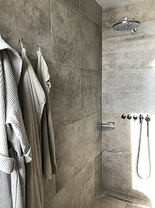 Begehbare Dusche mit Natursteinfliesen, Regenbrause und Bademänteln an der Wand.