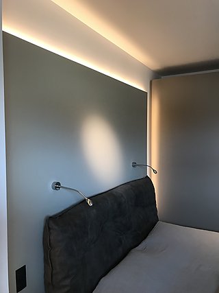 Schlafzimmer mit gepolstertem Betthaupt, Leseleuchten und indirekter Deckenbeleuchtung.