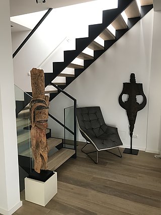 Offene Treppe mit afrikanischer Holzskulptur, Lounge-Sessel und Bronzefigur.